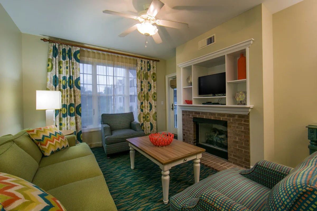 A bright and cheerful living room featuring a vibrant green sofa, colorful curtains that frame sunlit windows, a stylish coffee table with a decorative bowl, and a cozy fireplace beneath a sleek TV unit. The morning sunlight fills the space, creating a warm and inviting atmosphere perfect for family gatherings and relaxation.