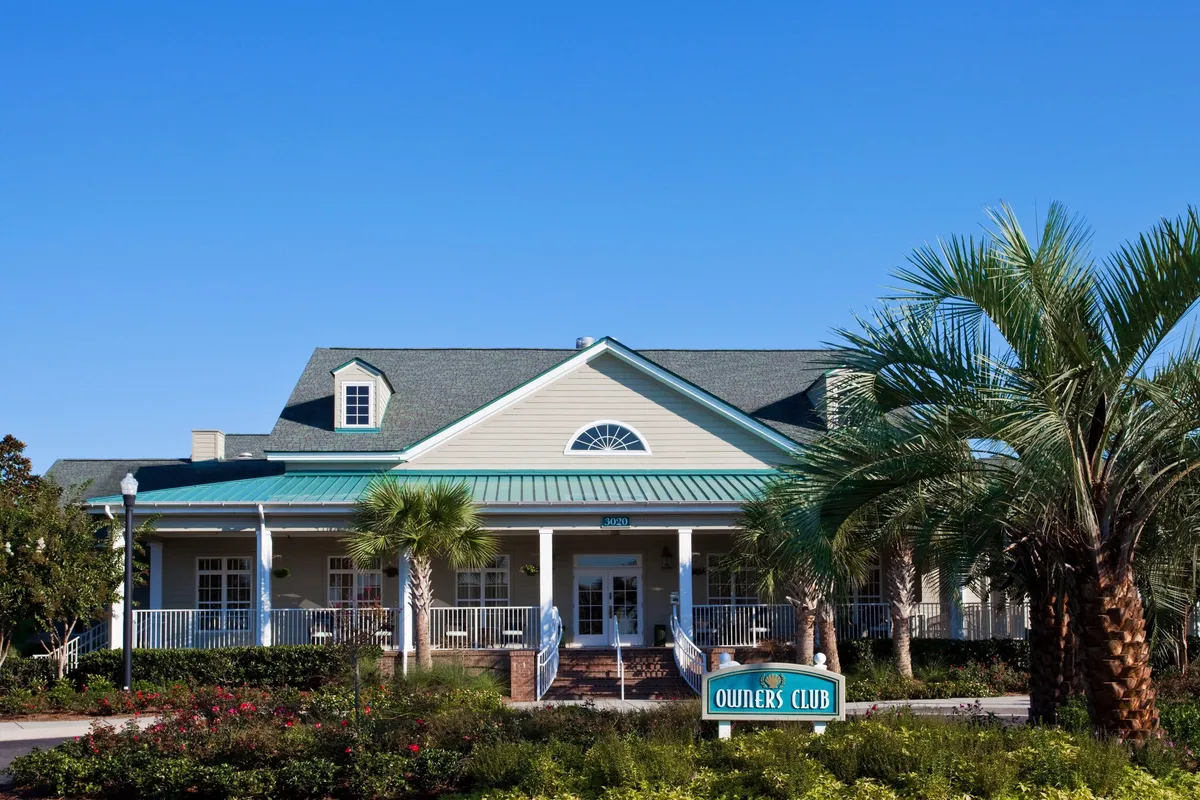 This image captures the welcoming main entrance of the Owners Club, set amidst lush palm trees and colorful flower beds. The prominent signage and inviting landscaping suggest a sense of arrival and community, while hints of gathering spaces imply opportunities for group interactions and social events.