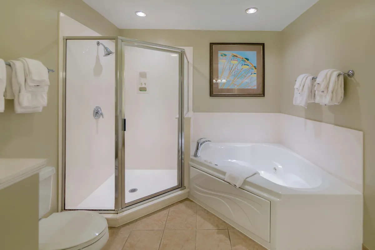 A tranquil bathroom scene with a large jacuzzi bathtub, a sleek shower enclosure, framed artwork, and neatly folded towels. The modern fixtures and the overall soothing ambiance evoke a spa-like experience, perfectly suited for relaxation and personal care.