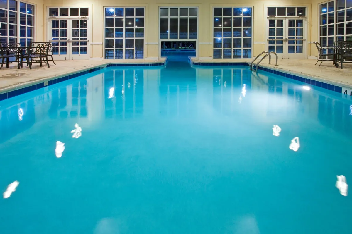 The serene indoor pool area showcases sparkling water, ample seating, and large windows letting in natural light. The mood is calm and inviting, perfect for relaxing swims or social time regardless of the weather outside.