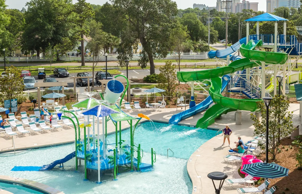 A lively outdoor pool area featuring vibrant water slides and a children's splash zone, surrounded by loungers for relaxing. Kids are seen splashing in the water and racing down giant slides, while parents enjoy the sun and snacks by the poolside.