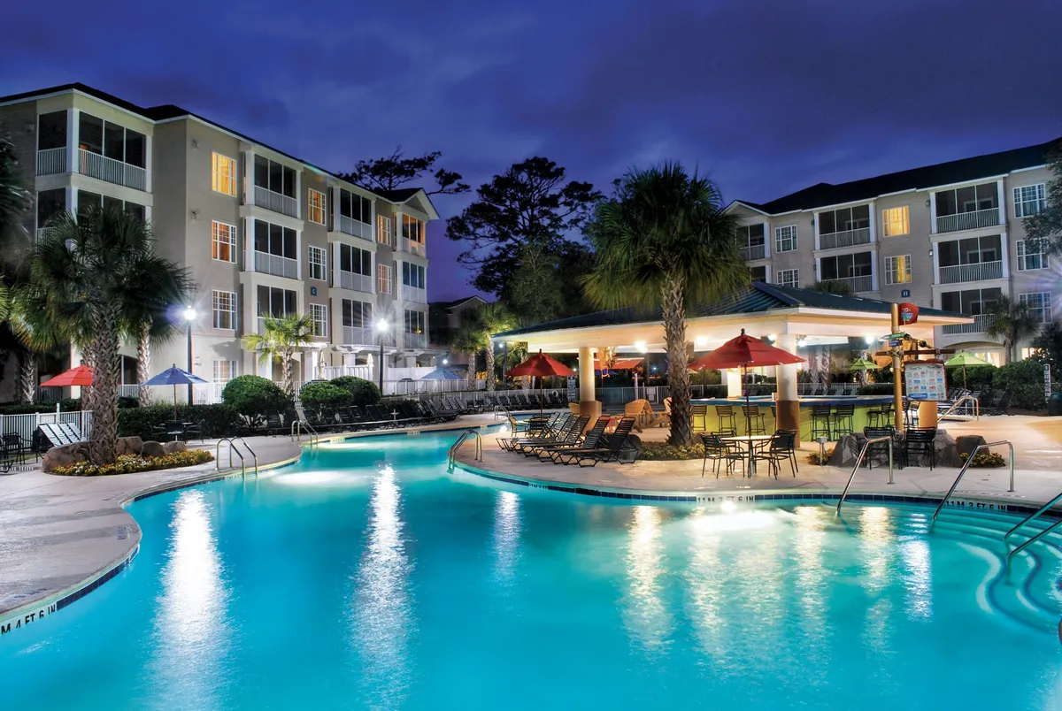 A stylish view of the Lagoon Pool at dusk, featuring an inviting outdoor bar area (Captain Cliff’s bar), umbrellas, and comfortable seating. The scene captures evening gatherings and a festive, tranquil mood.